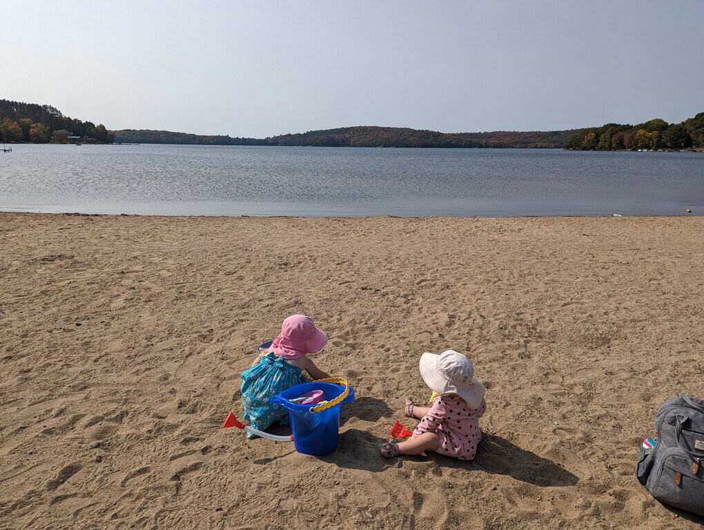 Two girls sitting on Doe Lake Beach in Katrine Ontario looking out over the lake on a summer day